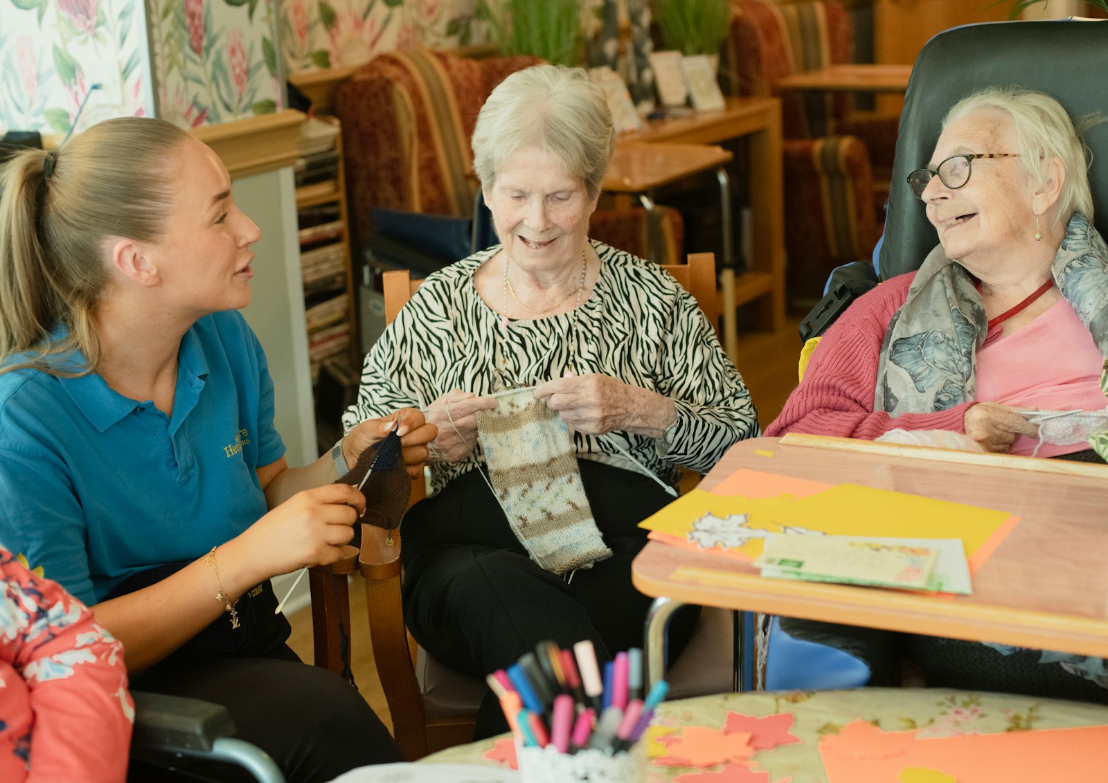 Caregiver assists two elderly women knitting